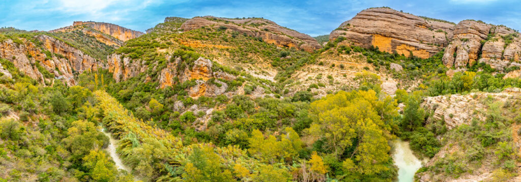 Paisaje del entorno de Alquézar, con un profundo barranco entre formaciones rocosas de tonos ocres y anaranjados, cubiertas de vegetación y atravesadas por un río.