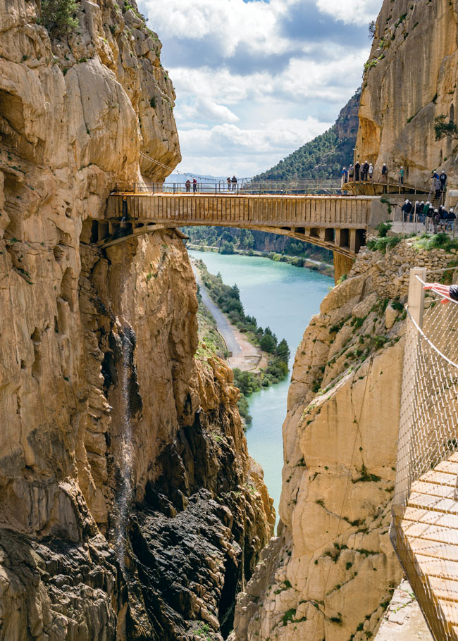 Vista del Caminito del Rey entre imponentes paredes de roca, con una pasarela suspendida sobre el desfiladero y el río de aguas turquesas al fondo.