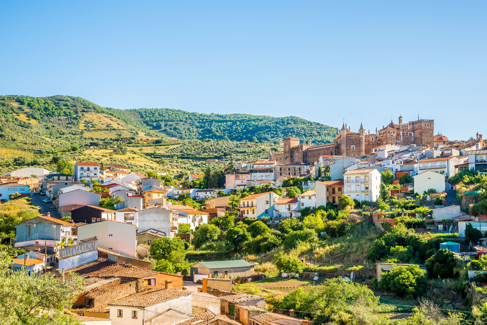 Vista panorámica de Guadalupe, en Extremadura, con sus casas blancas y el Real Monasterio de Guadalupe al fondo, rodeado de un paisaje de sierras y vegetación.