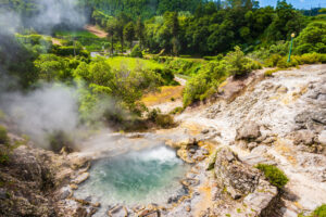 Paisaje termal de Furnas, en São Miguel, con una poza de aguas humeantes rodeada de rocas volcánicas y abundante vegetación.