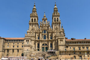 Fachada barroca de la Catedral de Santiago de Compostela, con sus dos grandes torres ornamentadas, frente a la plaza y bajo un cielo azul despejado.