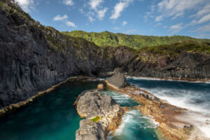Piscinas naturales de aguas cristalinas en la costa volcánica de las Azores, rodeadas de escarpadas paredes de roca y vegetación.