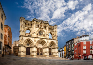 Catedral de Cuenca, de estilo gótico, con su elaborada fachada y rosetón, situada en una plaza del casco histórico junto a las coloridas casas tradicionales.