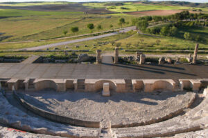 Restos de un antiguo teatro romano en el yacimiento arqueológico de Segóbriga, con las gradas y estructuras de piedra frente al paisaje rural de Castilla-La Mancha.