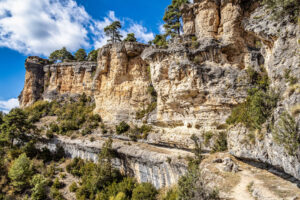 Paisaje rocoso de la Serranía de Cuenca, con imponentes formaciones de roca caliza, pinos y vegetación autóctona bajo un cielo azul.