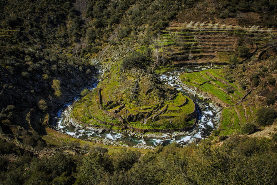Paisaje de Las Hurdes, con un río de aguas rápidas que serpentea entre formaciones rocosas, terrazas de cultivo y laderas cubiertas de vegetación.